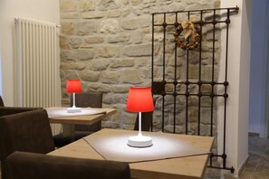 A room with a stone wall, a radiator, a metal gate with a wreath, and two tables with lamps. - Montis (San Massimo)