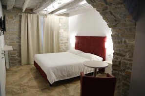 A bedroom with a stone wall, a bed with white bedding, a red headboard, and a small round table. - Montis (San Massimo)