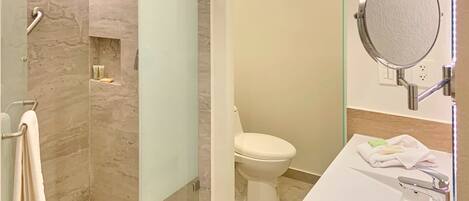 A modern bathroom with a glass-enclosed shower, a white toilet, and a sink with a mirror.