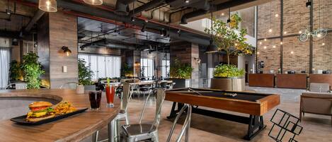 A modern bar area with a pool table, bar stools, and a burger on the counter.
