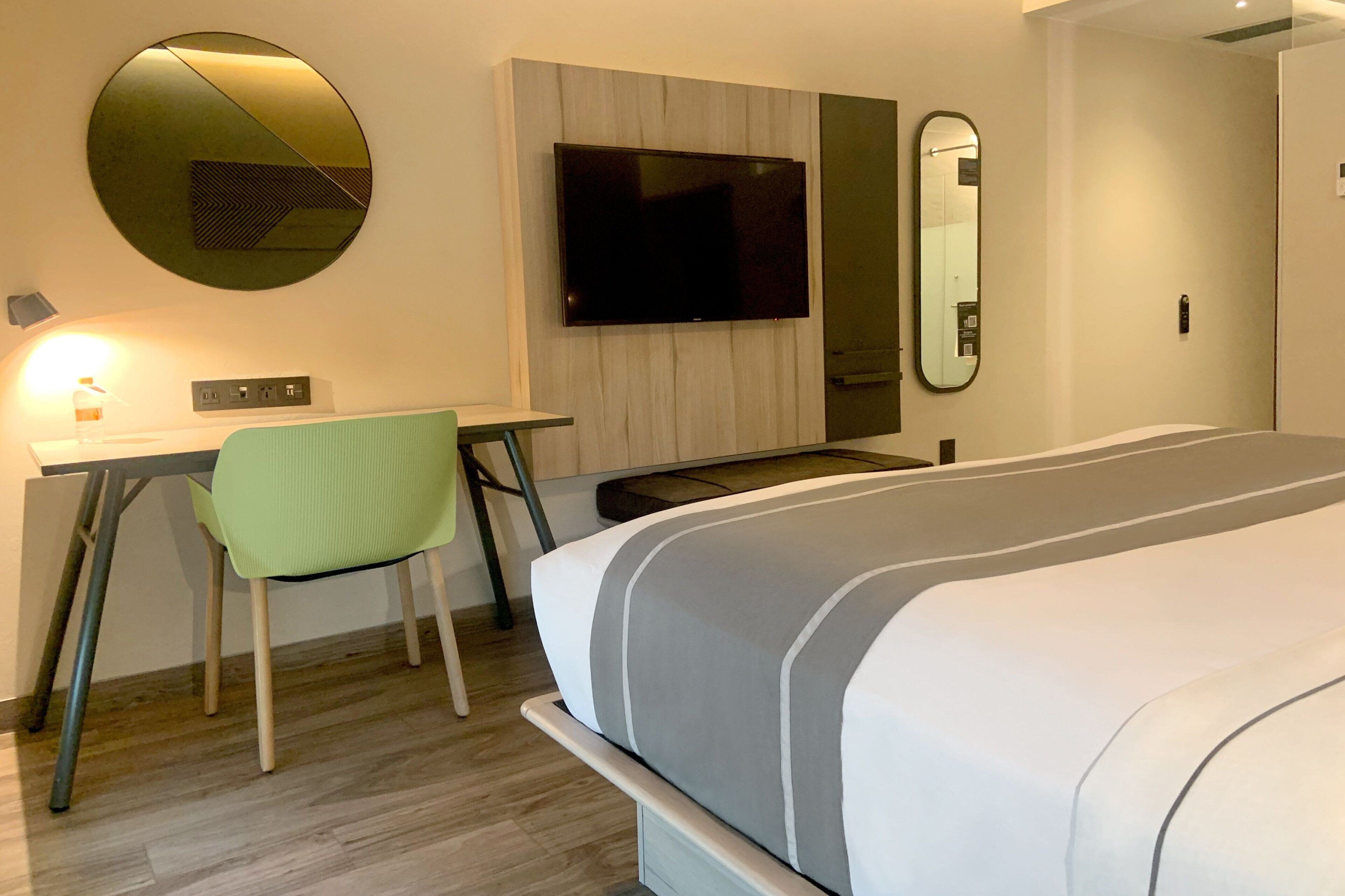 Une chambre d’hôtel moderne équipée d’un lit, d’un bureau, d’une chaise, d’une télévision et d’un miroir.