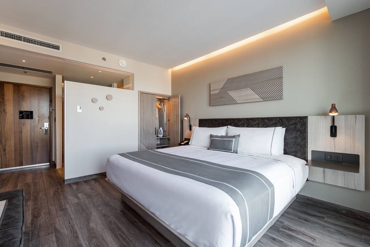 Ein modernes Hotelzimmer mit einem großen Bett, einem Holzschrank, einem Spiegel und einer Wandleuchte.