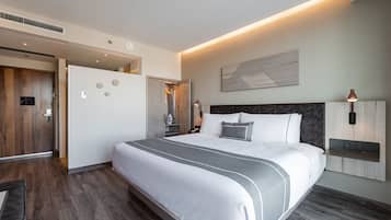 Quarto de hotel moderno com uma cama grande, um guarda-roupa de madeira, um espelho e uma luminária fixada na parede.