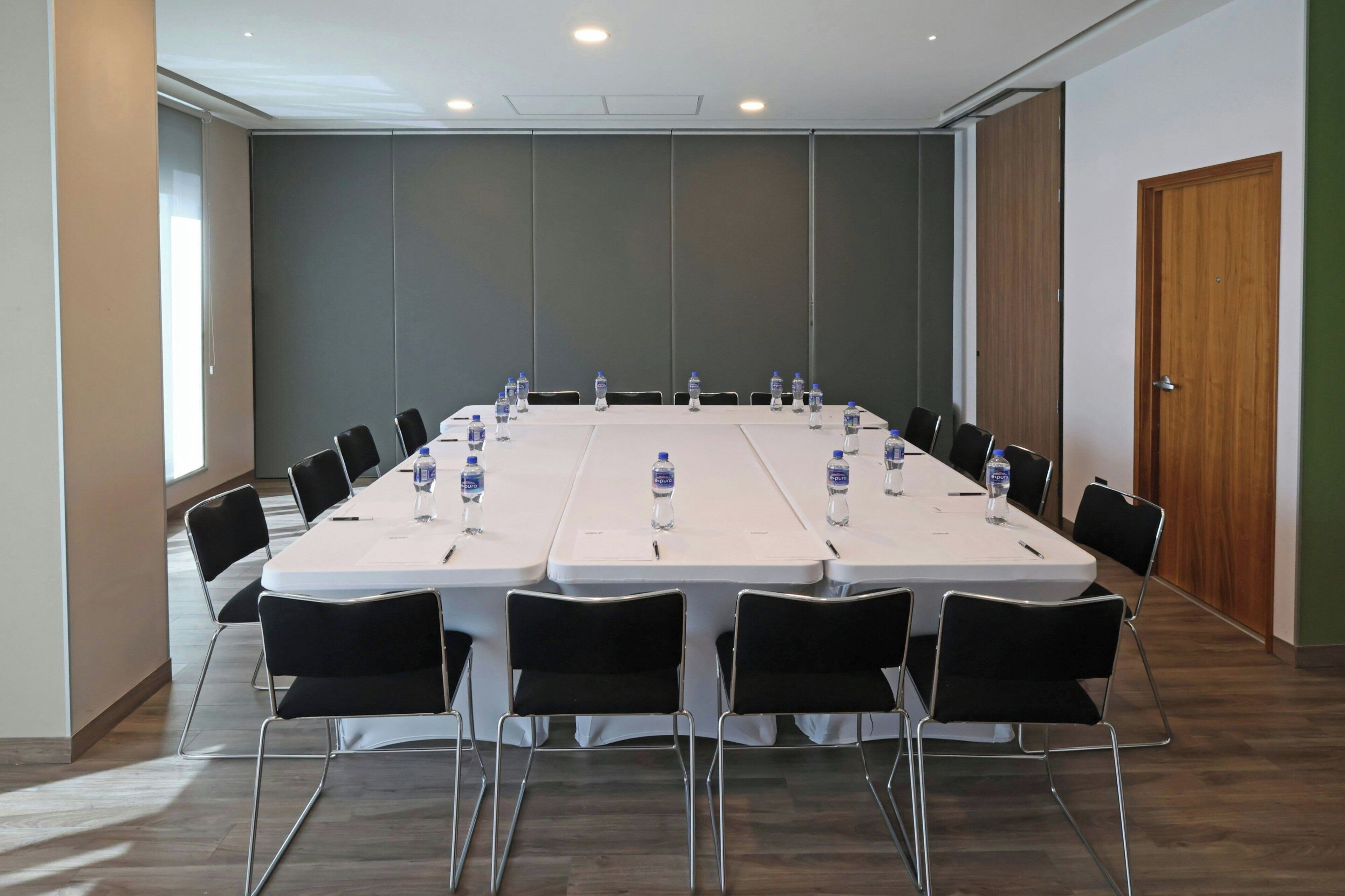 A conference room with a long table, black chairs, and water bottles.