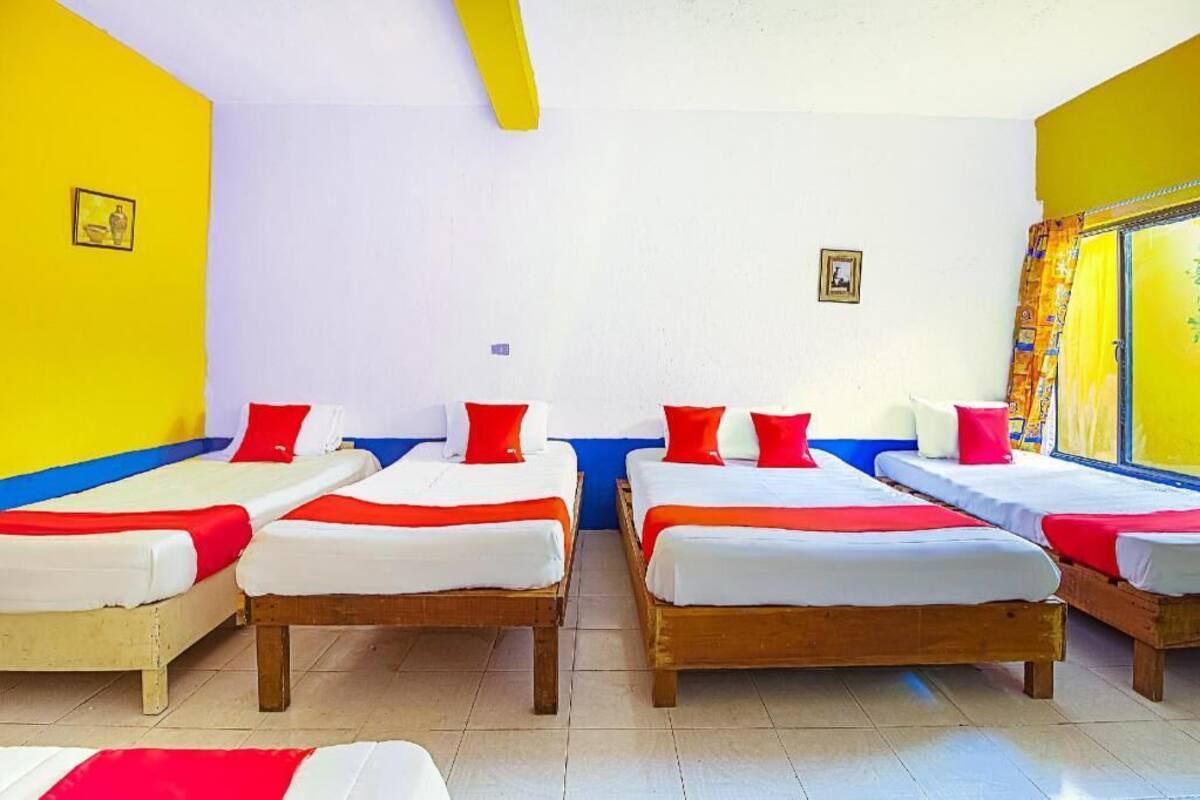 A room with four beds arranged in a row, each with white bedding and red pillows.