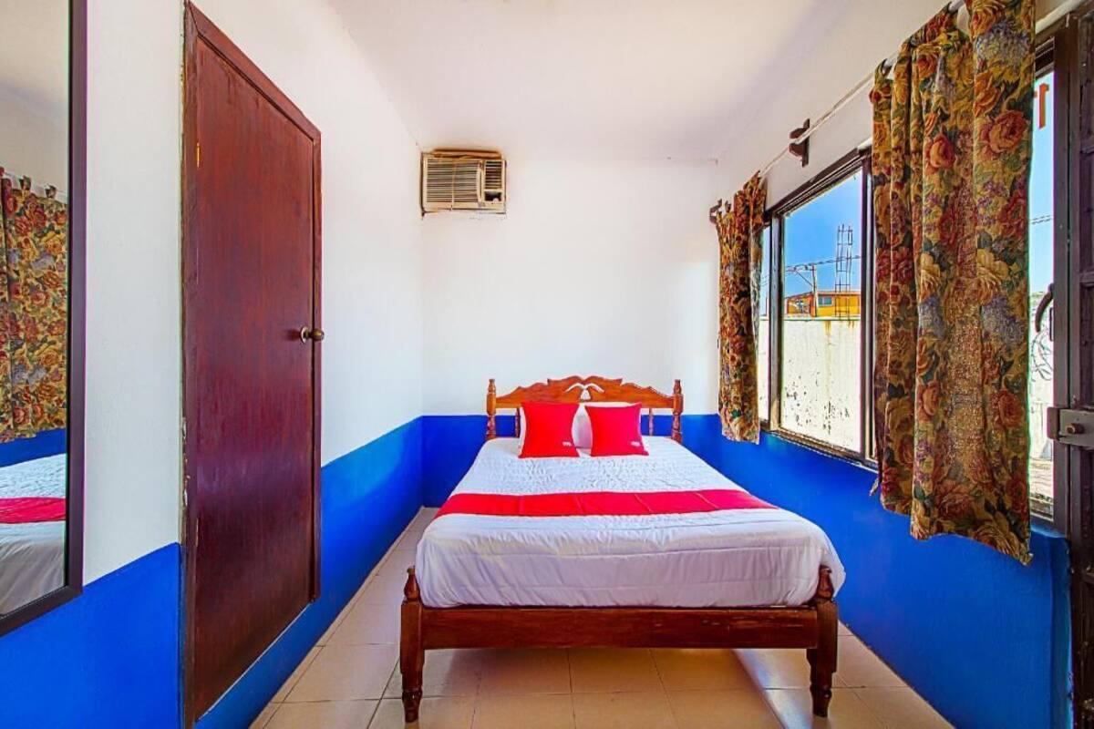 A bedroom with a wooden bed, a window with curtains, a door, and a wall-mounted air conditioning unit.