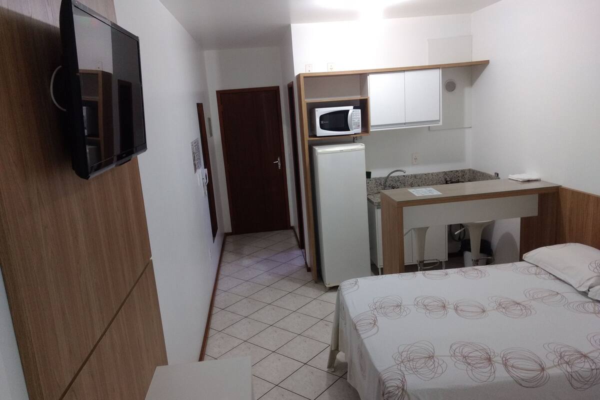 A compact hotel room with a bed, a desk, a microwave, and a small kitchenette.