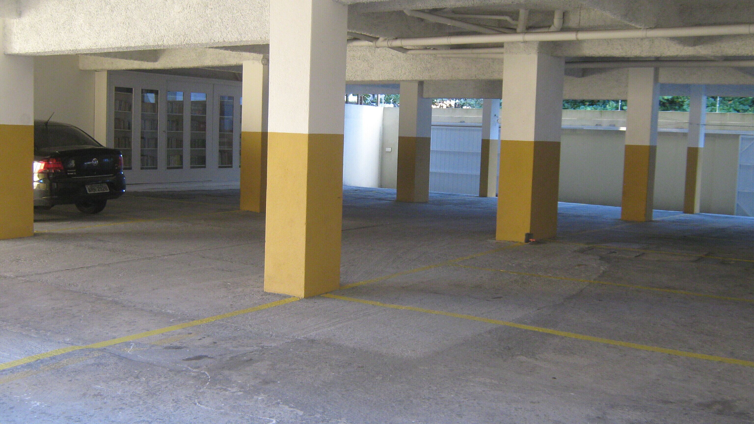 Un parking souterrain vide, avec des piliers jaunes et blancs, un sol en béton et une voiture garée au fond.