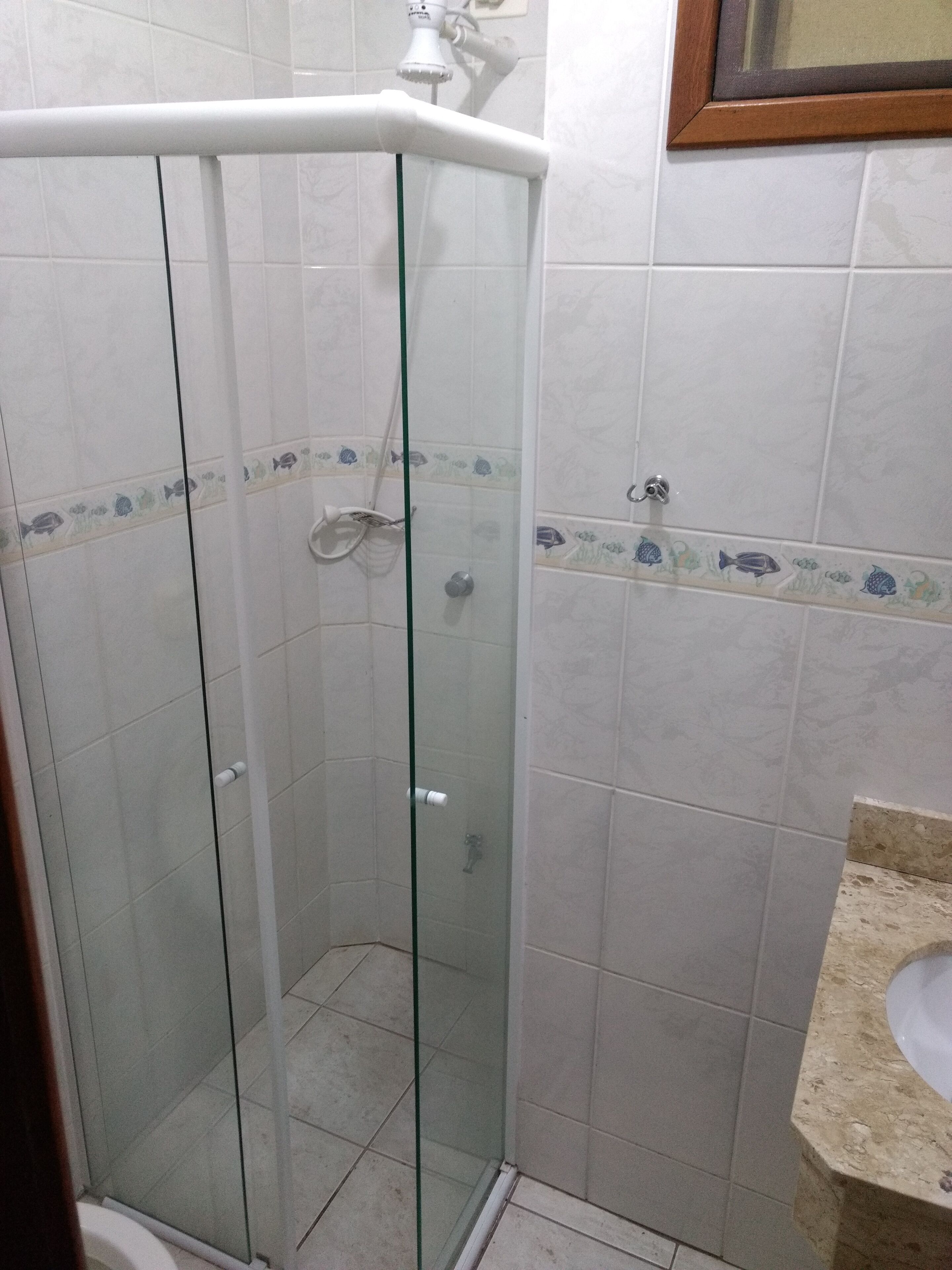 Eine Duschkabine mit Glas, eine weiße Toilette und ein Waschbecken mit einer beige gefärbten Arbeitsplatte.