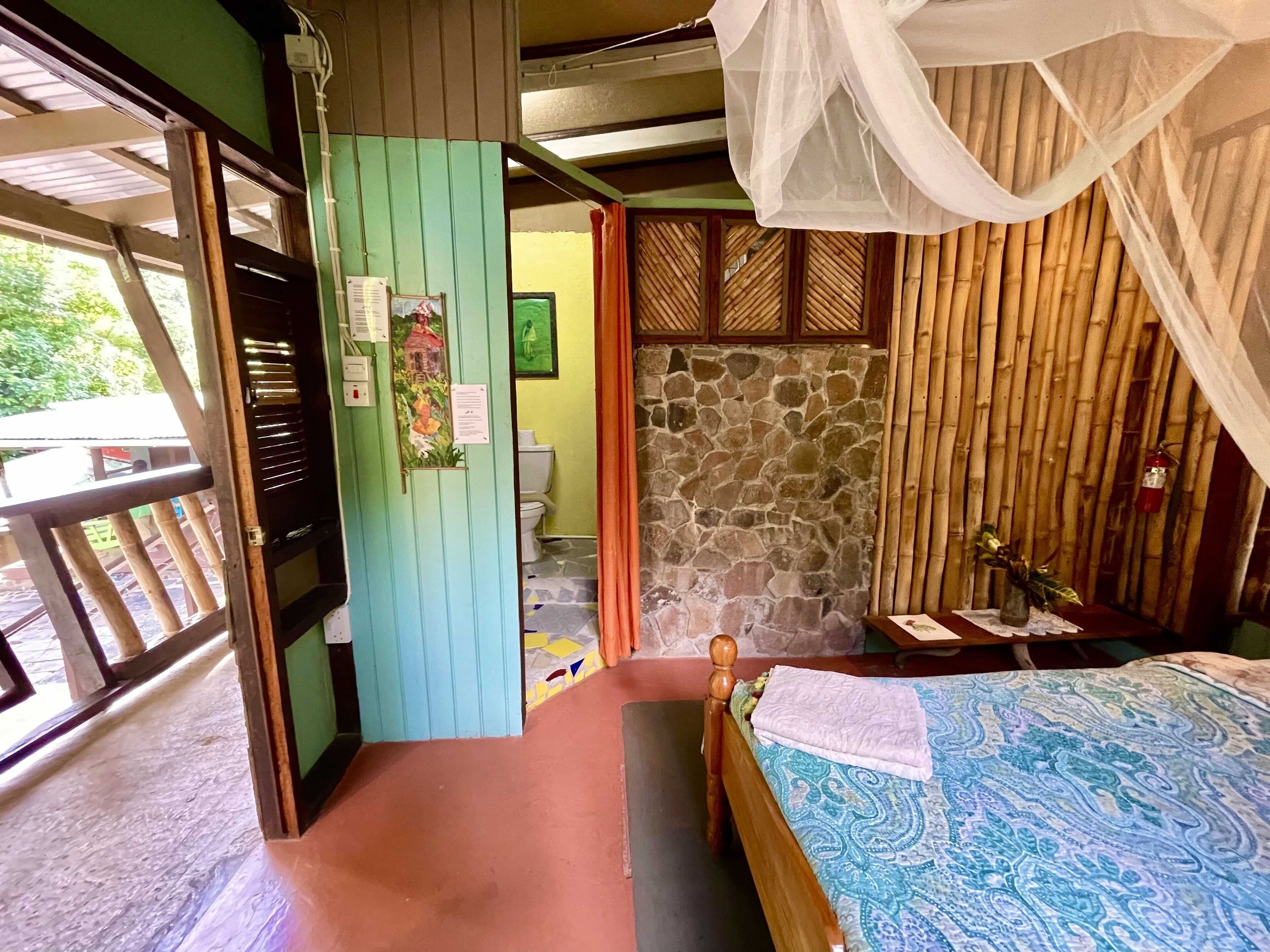 A room with a bed, a wooden door, a stone wall, and a bamboo fence.