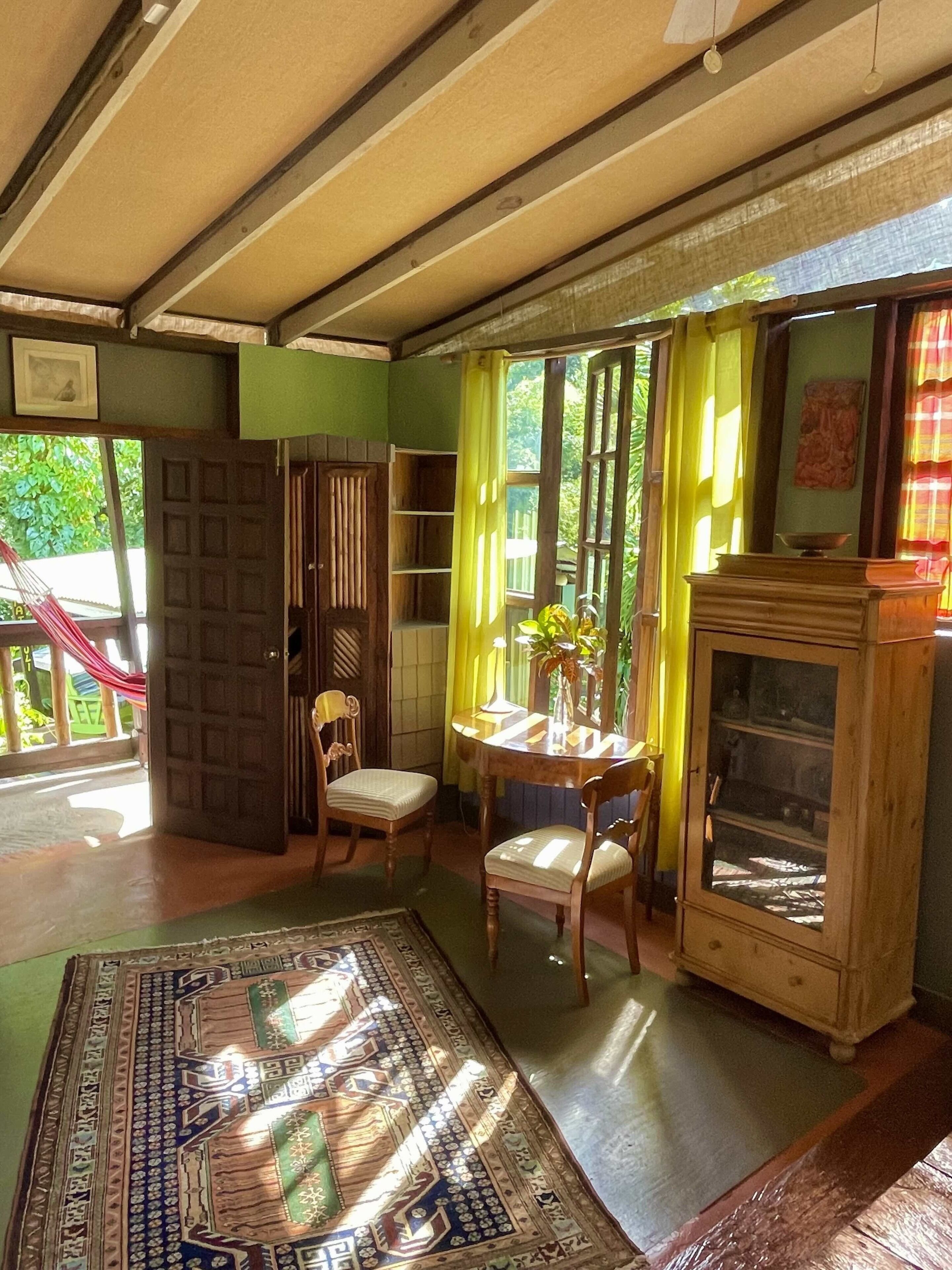 A room with a wooden floor, a patterned rug, a wooden cabinet, and a dining table with chairs.
