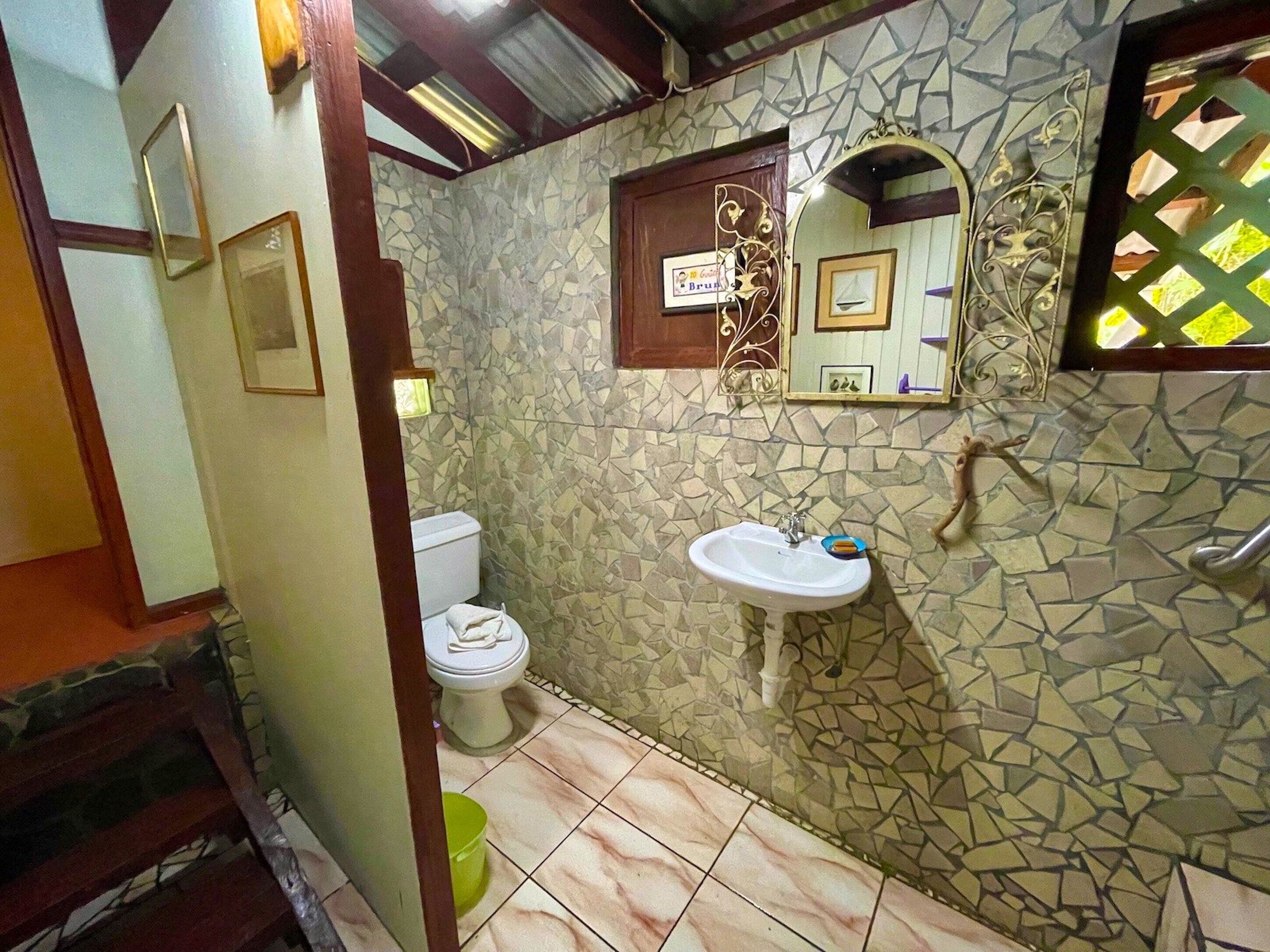 A bathroom with a mosaic wall, a toilet, a sink, and a mirror.