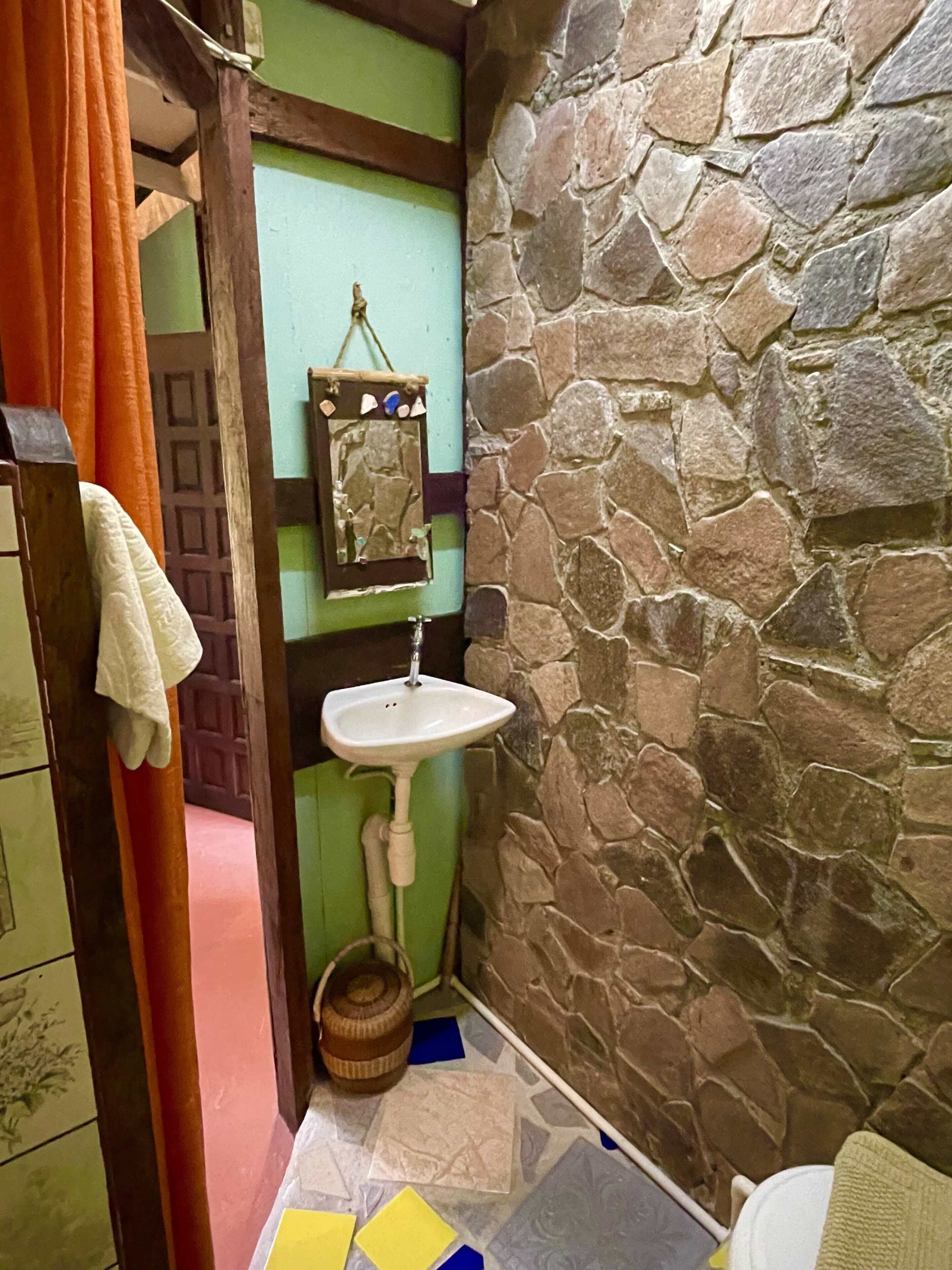 Un baño con pared de piedra, puerta verde, lavamanos blanco y espejo con marco decorativo.