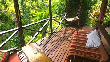 A wooden deck with a hammock and a cushioned bench, overlooking a lush green forest.