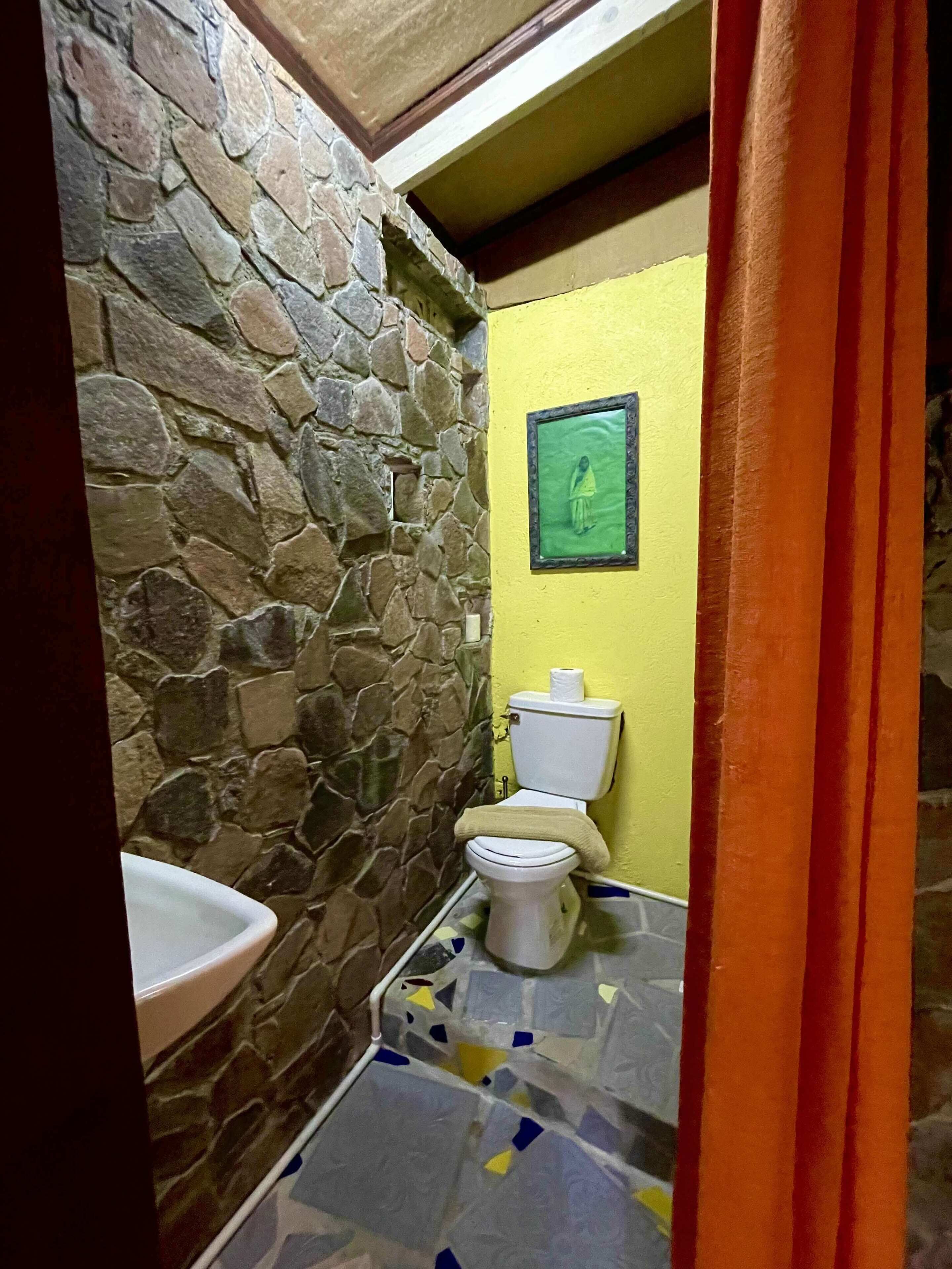 A bathroom with a stone wall, a yellow wall, a toilet, and a sink.