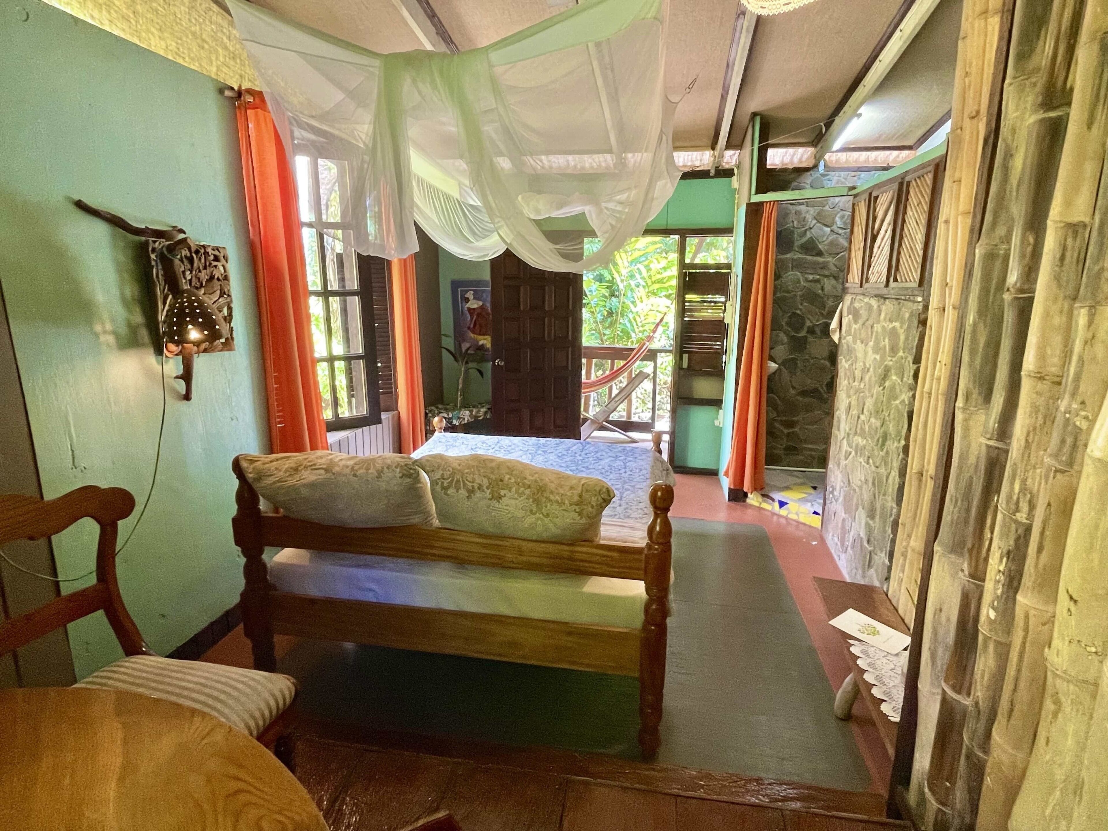 A room with a bed, a chair, a hammock, and a view of the outdoors.