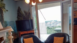 A living room with a sofa, a coffee table, a TV, and a balcony with a view.
