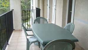 A balcony with a green table and chairs, a tiled floor, and a view of greenery.