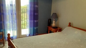A bedroom with a wooden bed, a nightstand with a lamp, and a view of a balcony with blue curtains.