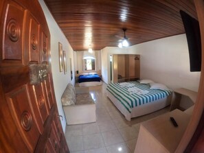 A hotel room with a wooden ceiling, a bed with a striped bedspread, a sofa, a TV mounted on the wall, and a door with a sign. - Hotel Rural Vale das Nascentes (Salesopolis)