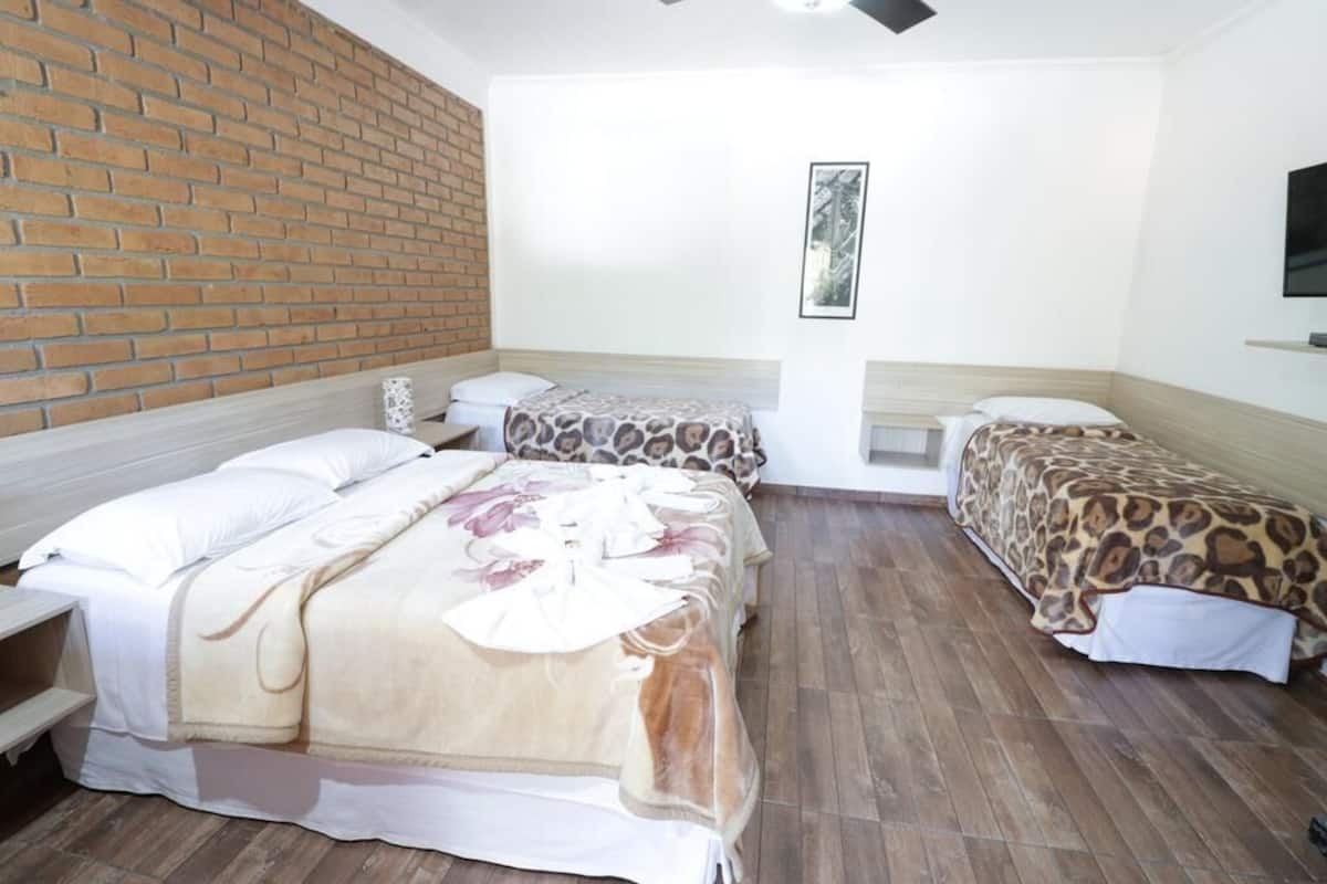 Une chambre d’hôtel avec deux lits, un mur en briques, un tableau encadré et un téléviseur fixé au mur.