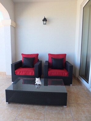 Two wicker sofas with red cushions and black pillows, a glass coffee table, and a wall-mounted lantern.