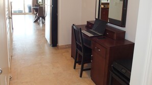 Hotellihuoneessa on työpöytä, tuoli ja suuri peili. Taustalla näkyy ruokailutila, jossa on pöytä ja tuoleja.
