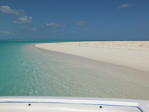 Ein Strand mit klarem türkisblauem Wasser und weißem Sand, Blick vom Boot aus.