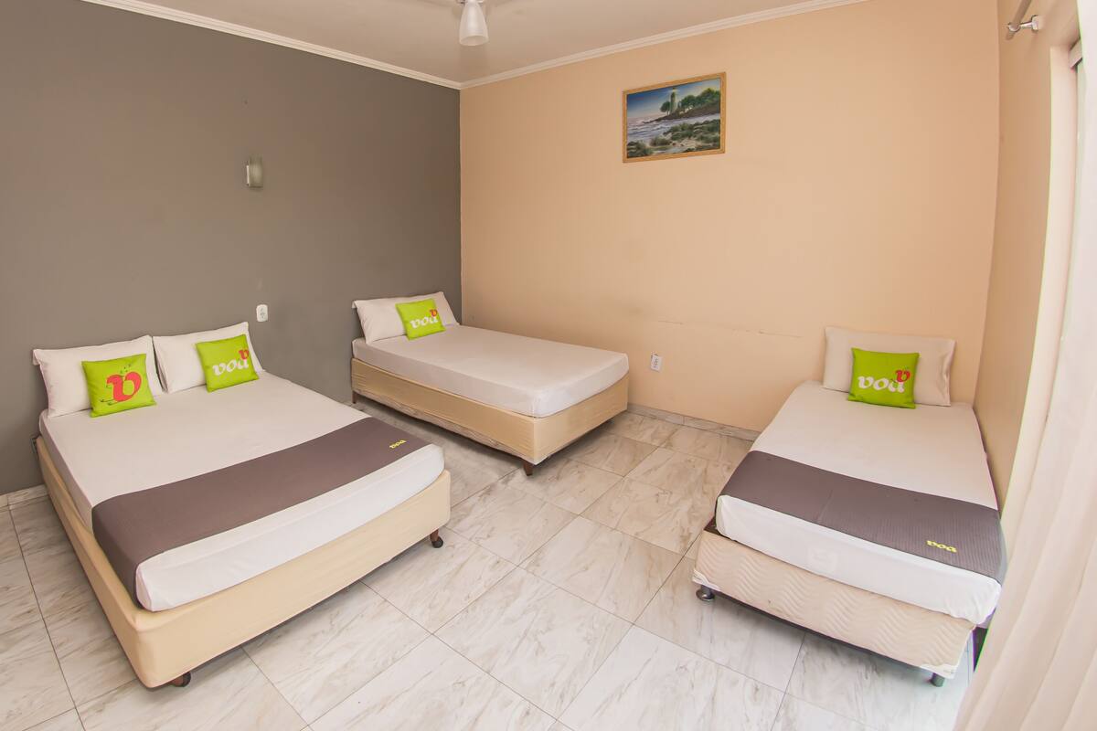 Habitación de hotel con tres camas, cada una con colchón y almohadas, y un cuadro en la pared.