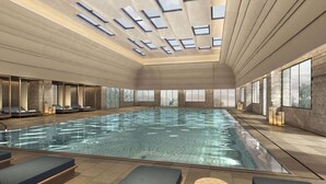 Een modern binnenzwembad met glazen wanden, een verlicht plafond en comfortabele lounges met kussens.