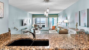 A kitchen with a granite countertop and a sink, a dining area with a table and chairs, and a living room with a sofa and a coffee table. - Seaside Beach House 201 · 2 Full Baths · Gulf Front (Holmes Beach)