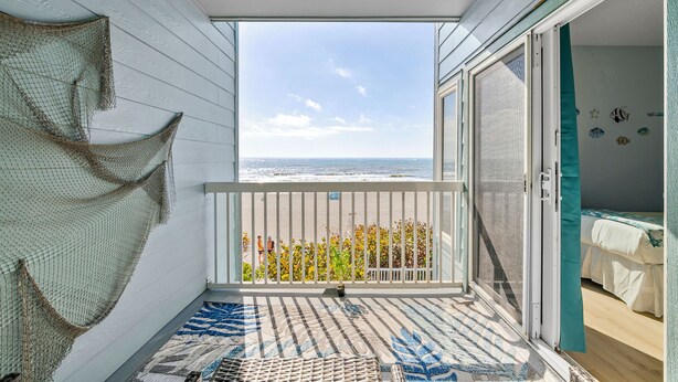 A balcony with a view of the beach, a ceiling fan, and a bed with a view. - Seaside Beach House 201 · 2 Full Baths · Gulf Front (Holmes Beach)