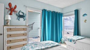 A bedroom with a view of the beach, a dresser, two beds, and a window with curtains. - Seaside Beach House 201 · 2 Full Baths · Gulf Front (Holmes Beach)