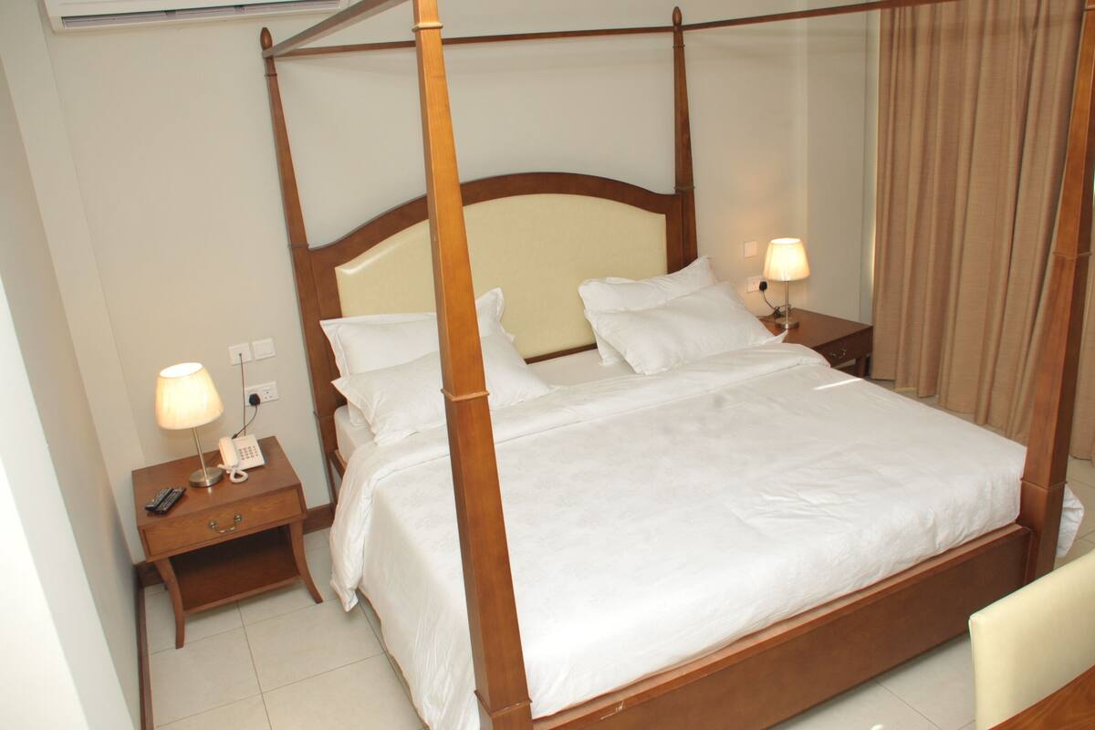 A four-poster bed with white linens, two bedside tables with lamps, and a wooden headboard.