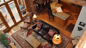 Un vaste espace de vie comprenant un canapé en cuir, une table basse et un tapis. On y trouve également un coin repas avec une table et des chaises, ainsi qu’une cuisine dotée d’un plan de travail en granit.