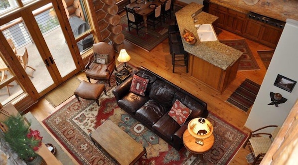 Un vaste espace de vie comprenant un canapé en cuir, une table basse et un tapis. On y trouve également un coin repas avec une table et des chaises, ainsi qu’une cuisine dotée d’un plan de travail en granit.