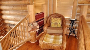 L’intérieur d’une cabane en rondins, avec un fauteuil en osier, un escalier en bois et une petite table.
