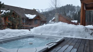 Une cabane en bois avec un jacuzzi, le tout entouré de neige.