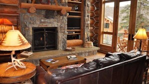 L’intérieur d’un chalet confortable, avec une cheminée en pierre, un canapé en cuir et des étagères en bois.