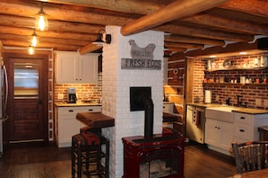 A rustic kitchen with a brick wall, wooden beams, a red stove, and a sign reading "BROIERS FRESH EGGS".