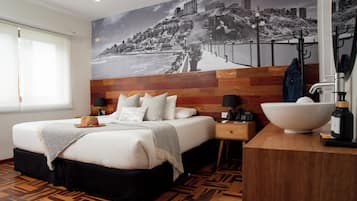 Habitación de hotel con cama, mesita de noche, ventana grande, espejo montado en la pared, piso de madera y un mural con vista a la ciudad.