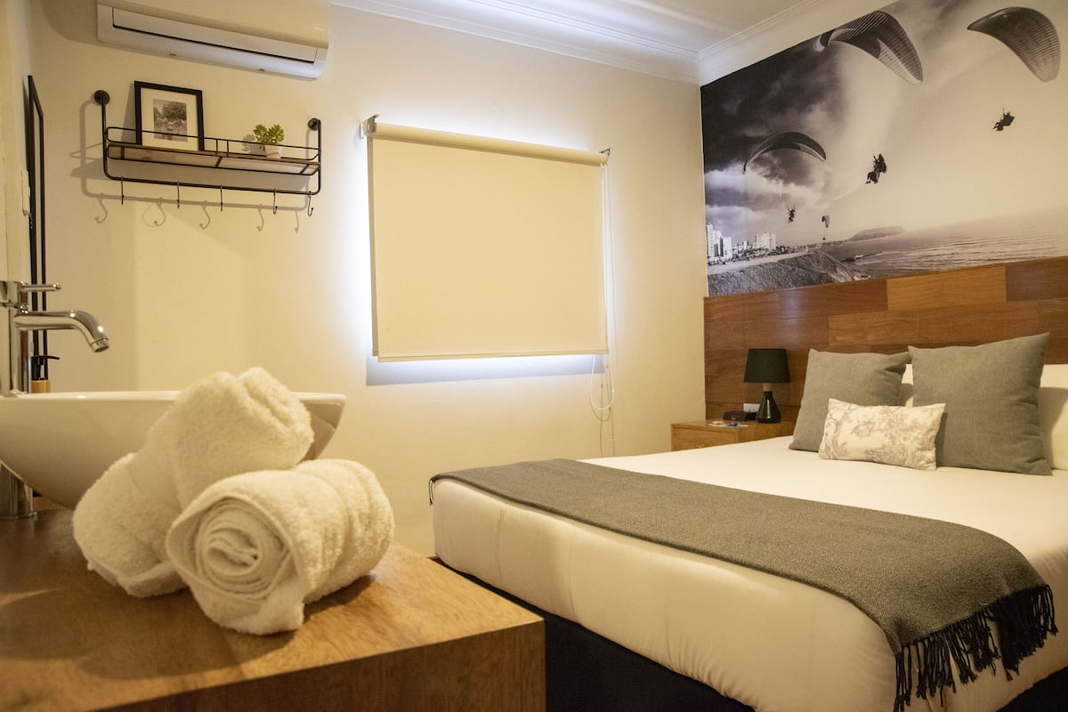 Habitación de hotel con una cama grande, un baño con bañera, una ventana con persiana y un mural en la pared.