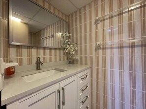 Ein Badezimmer mit gestreifter Tapete, einem weißen Waschbecken, einem Spiegel und einer Vase mit Blumen.