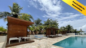 Area piscina con cabanas in legno e poltrone relax, una piscina limpida blu e palme circostanti.