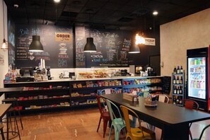 Ein Café mit einer Kreidetafel, einer Theke voller Speisen, einem Getränkekühlschrank und bunten Stühlen.
