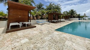 Ein Poolbereich mit Holz-Cabanas und Liegestühlen, einem klaren blauen Pool und umliegenden Palmen.
