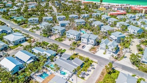 Vue aérienne d’une zone résidentielle côtière, avec des maisons, une plage et un ciel bleu dégagé.