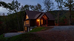 A rustic cabin with a sloped roof, wooden exterior, and a porch with a railing.