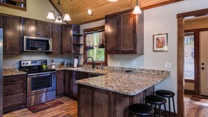 A kitchen with dark wood cabinets, stainless steel appliances, granite countertops, and a large island with bar stools.