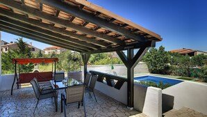 En udendørs terrasse med et bord, stole, en pergola og en swimmingpool.